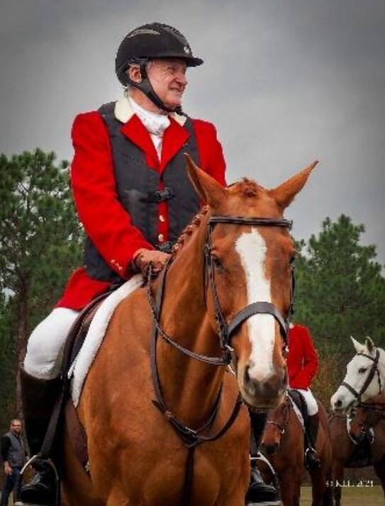 Man in red coat and helmet on braided chestnut horse.