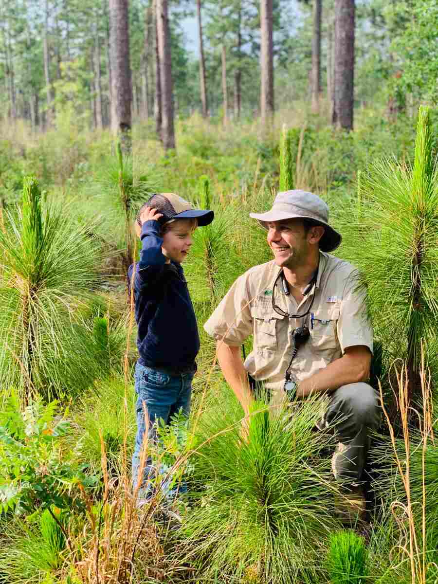 Man in khaki with small boy wearing blue in field of longleaf pines