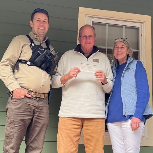 Two men and a woman, one holding a check.